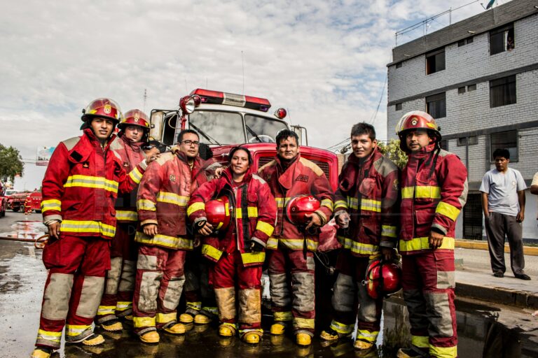 Brave firefighters in red uniforms pose in front of a fire truck on a city street in Chiclayo, Perú.