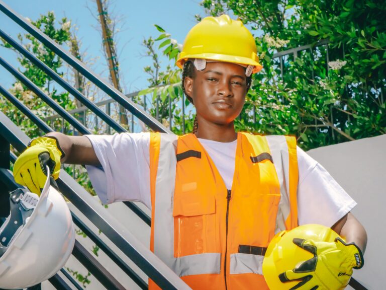 Confident construction worker wearing PPE and holding helmet on outdoor site.