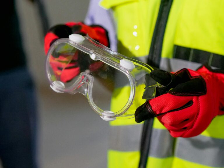 Close-up of a person holding safety goggles with protective gloves, featuring high visibility gear.